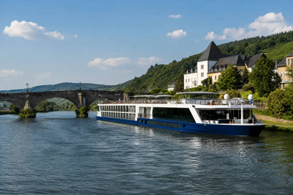 Flusskreuzfahrtschiff nähert sich mit abgesenktem Steuerhaus einer niedrigen Steinbrücke